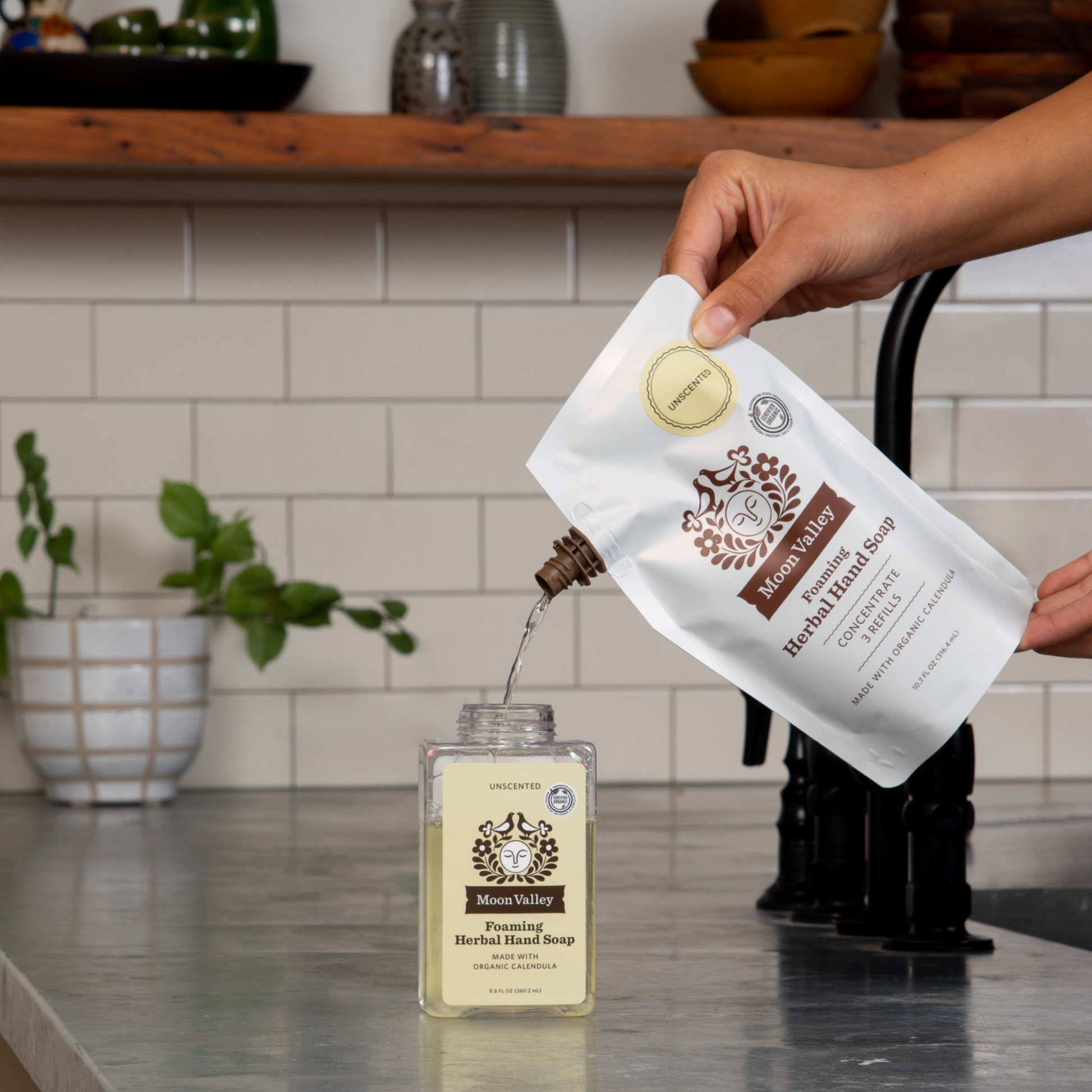 Moon Valley Organics Foaming Herbal Hand Soap Refill being poured into Foaming Herbal Hand Soap Dispenser Unscented on a kitchen sink