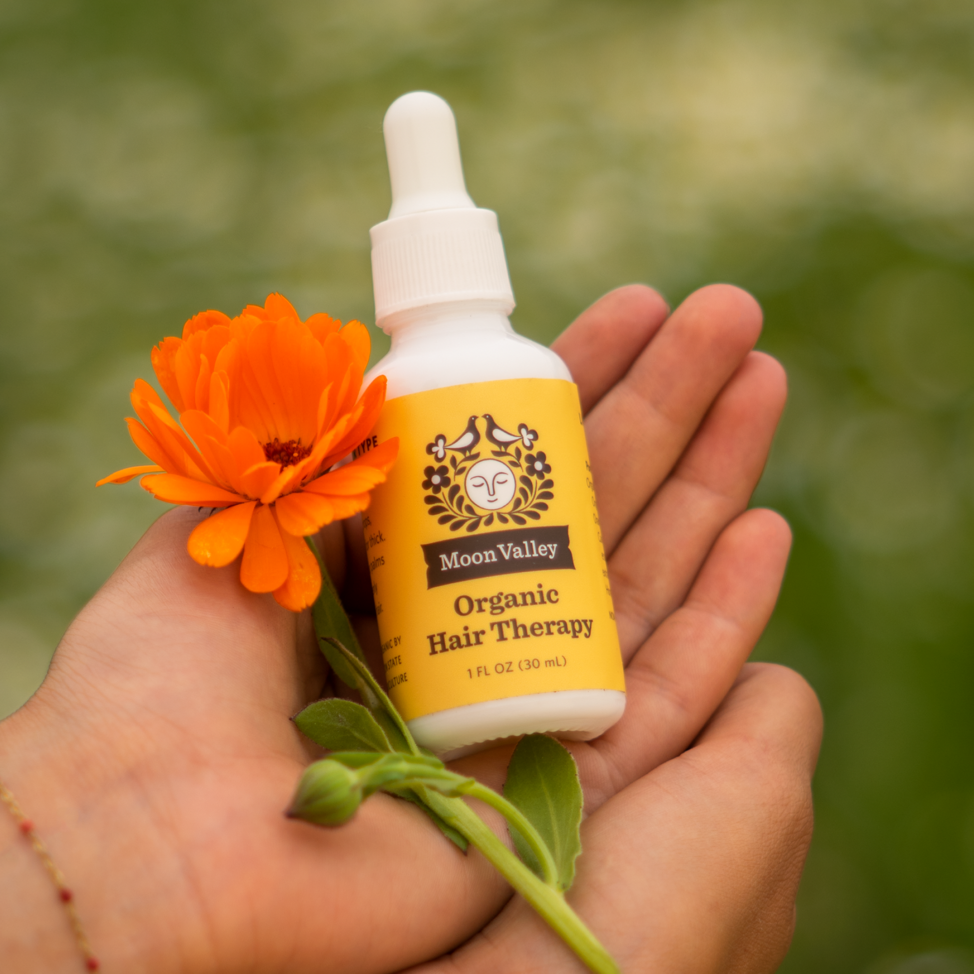 Moon Valley Organics Hair Therapy Every Type hand holding bottle with calendula flower